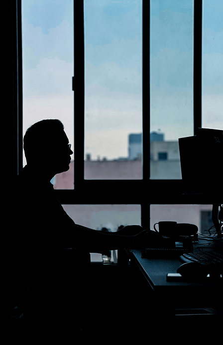 Silhouette of a person sitting at a desk by a window with a city view